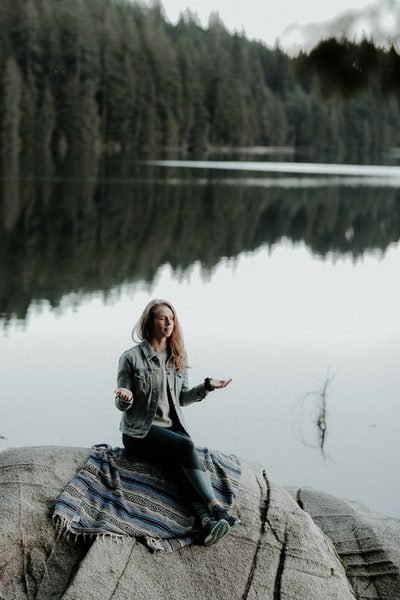 在湖岸岩石上冥想的女人